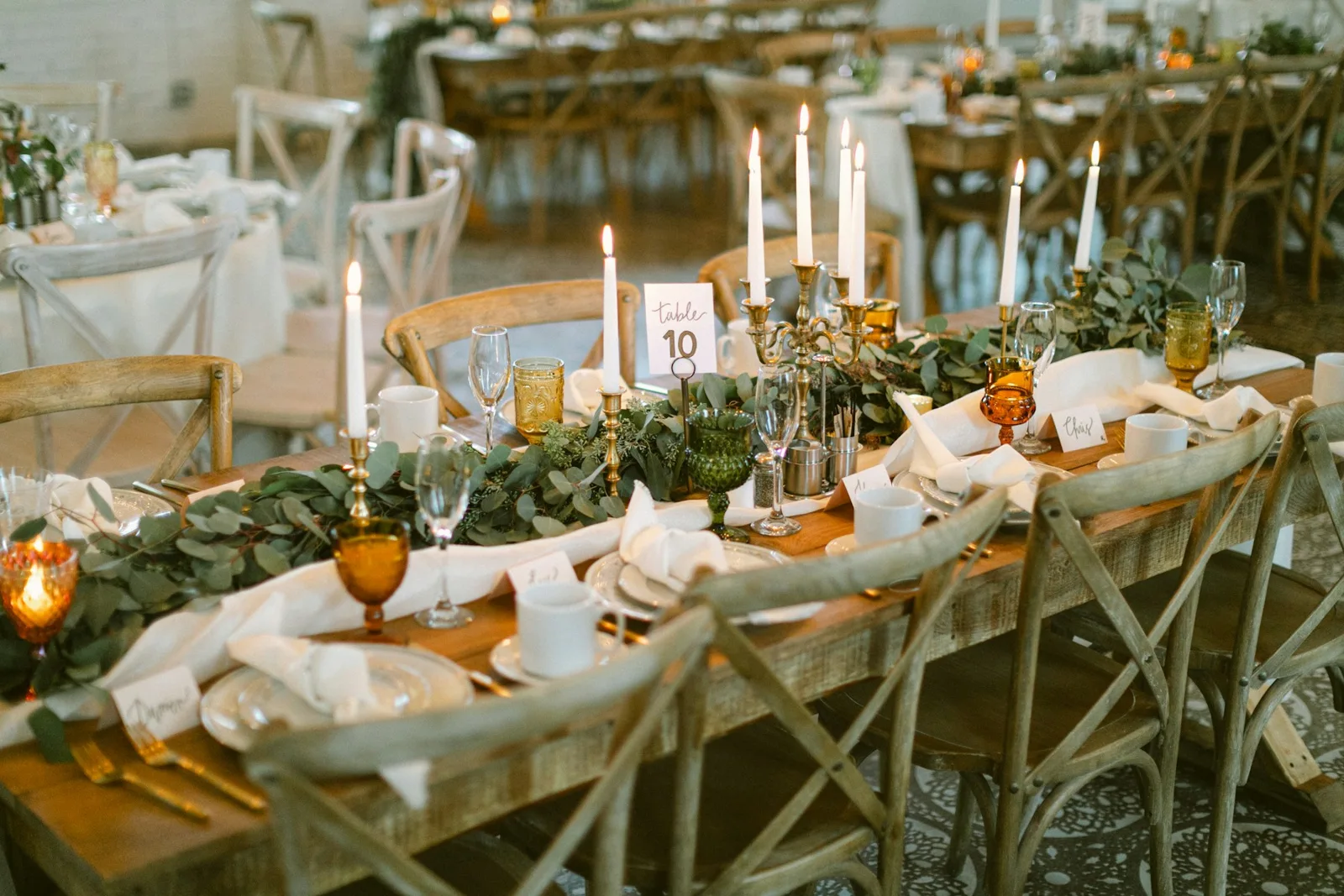 Candlelit wedding tables with greenery, amber glasses and warm wood details